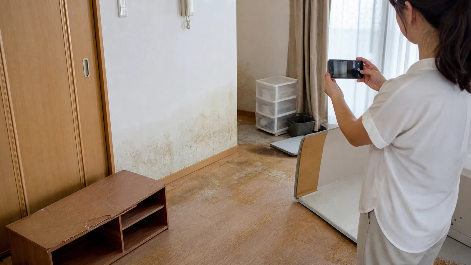 室内の水濡れ跡と傷んだ家具をスマートフォンで記録する住人。