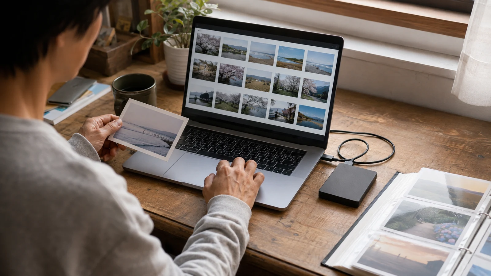 ノートパソコンの写真一覧と外付け保存機器を用い、家族に残す写真を確認する自宅の作業机。