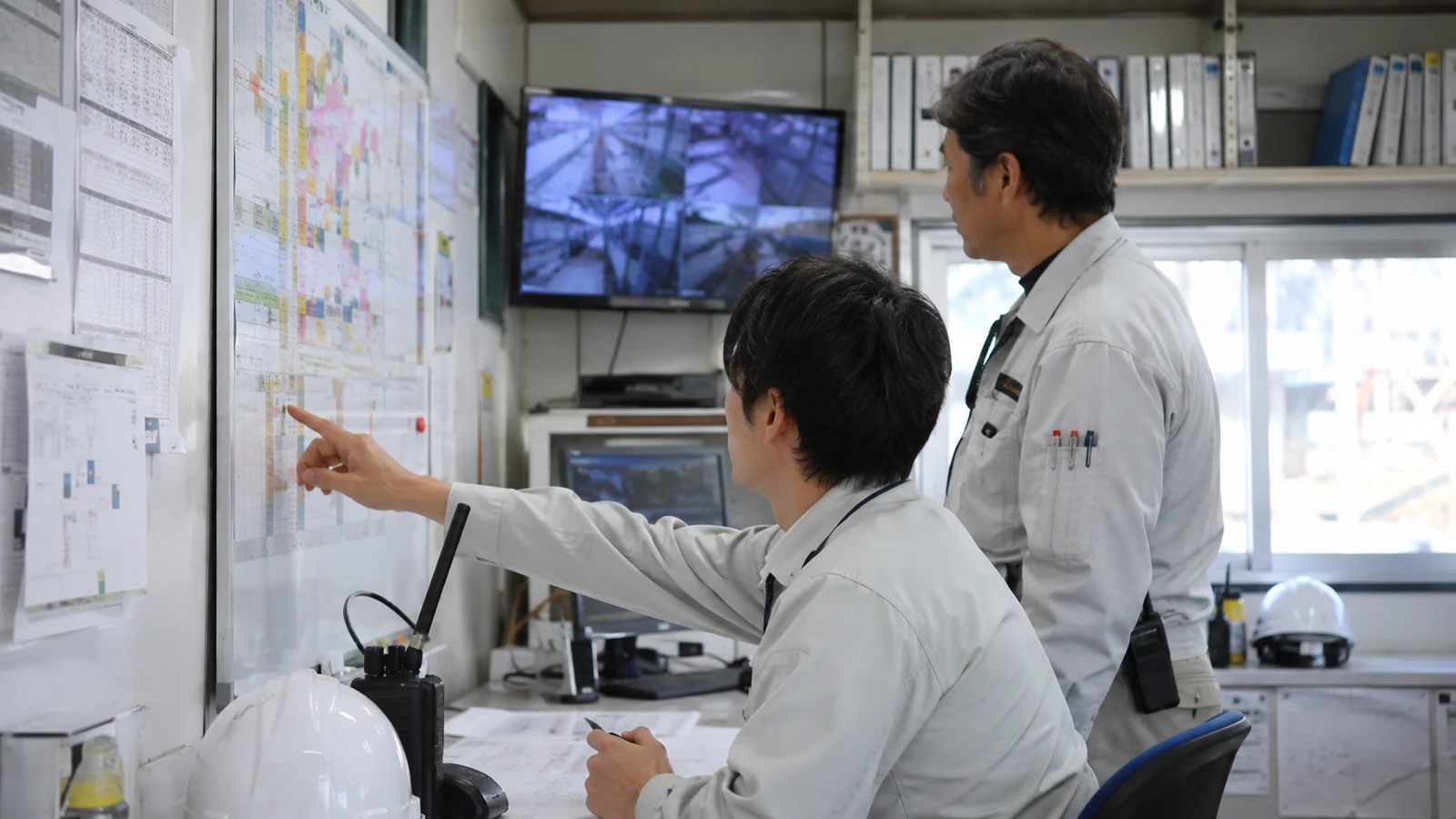 建設現場の連絡員と営業所技術者が、入退場、下請次数、通信、労働時間を人員配置計画書で更新している。