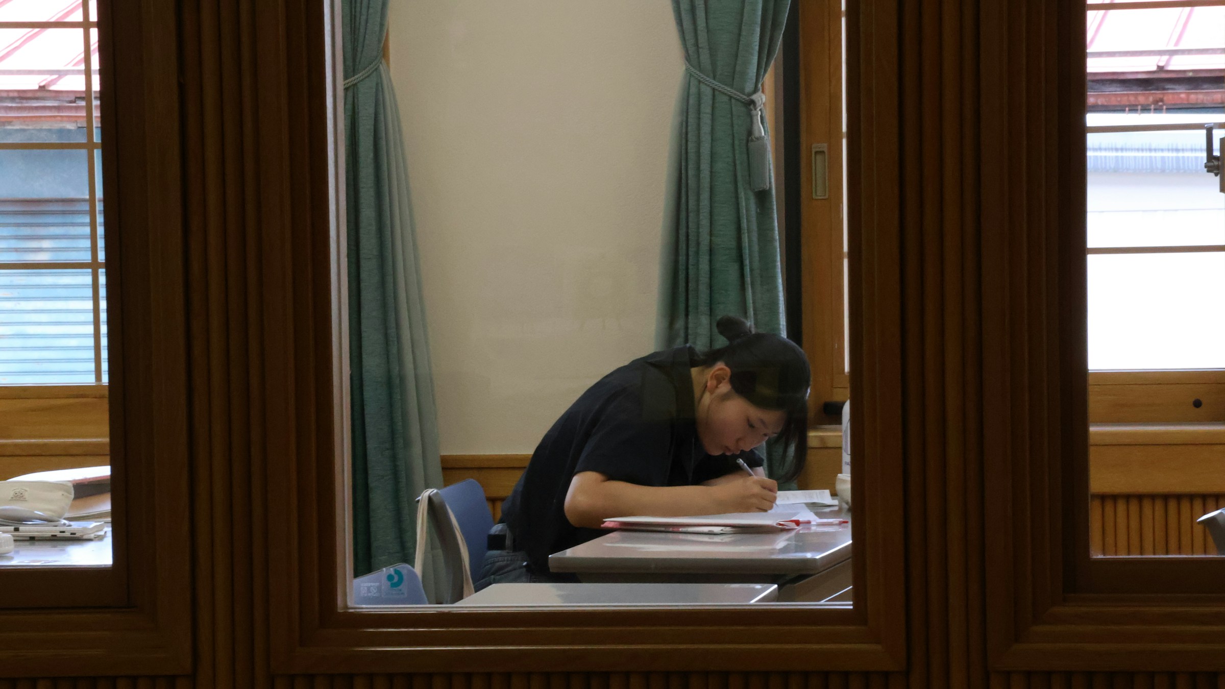 木枠の窓越しに、机で参考書に向かう学習者の姿。