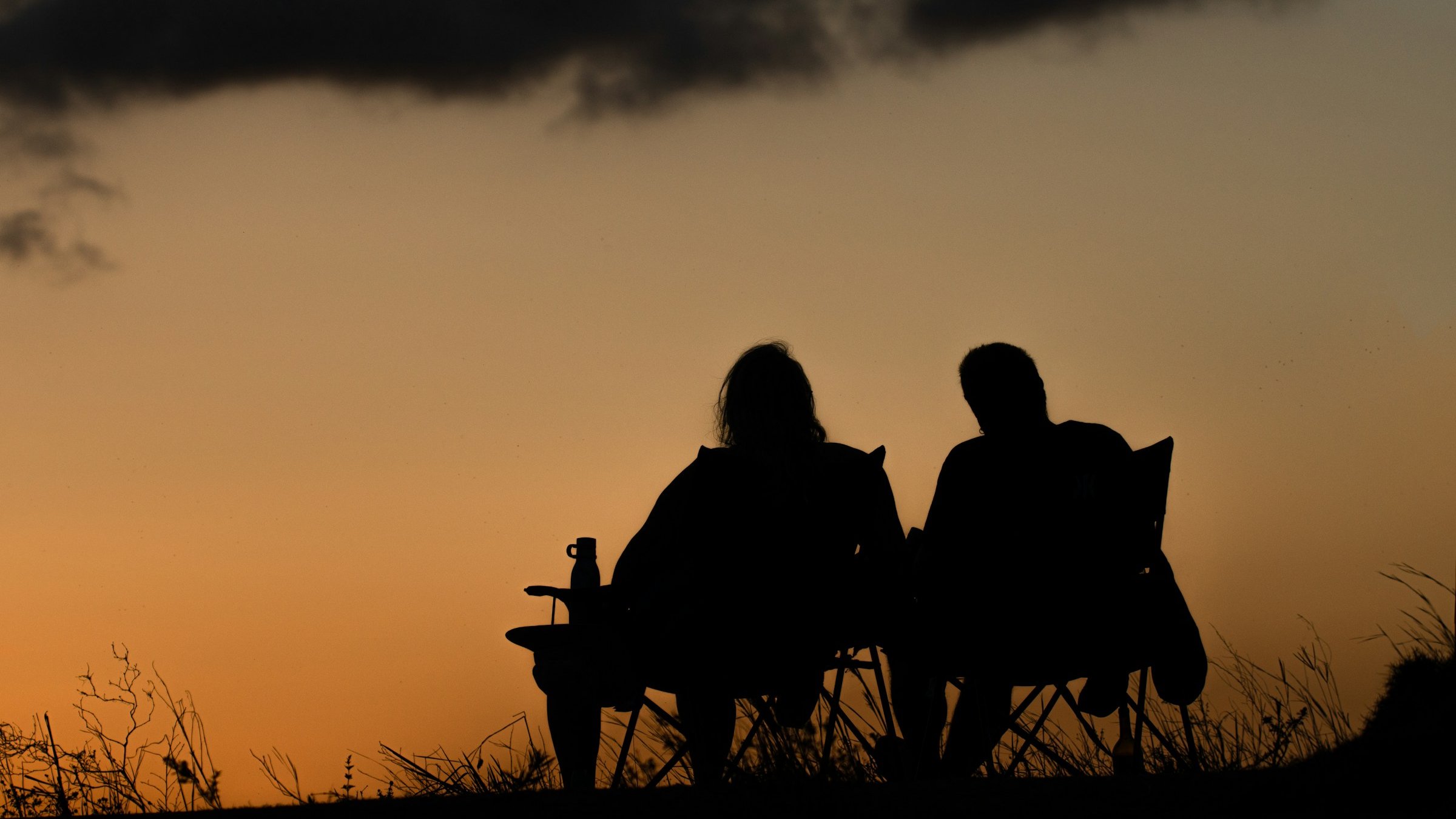 夕暮れのベンチに座る2人のシルエット。婚活=出会いの場面を象徴する静かな光景。