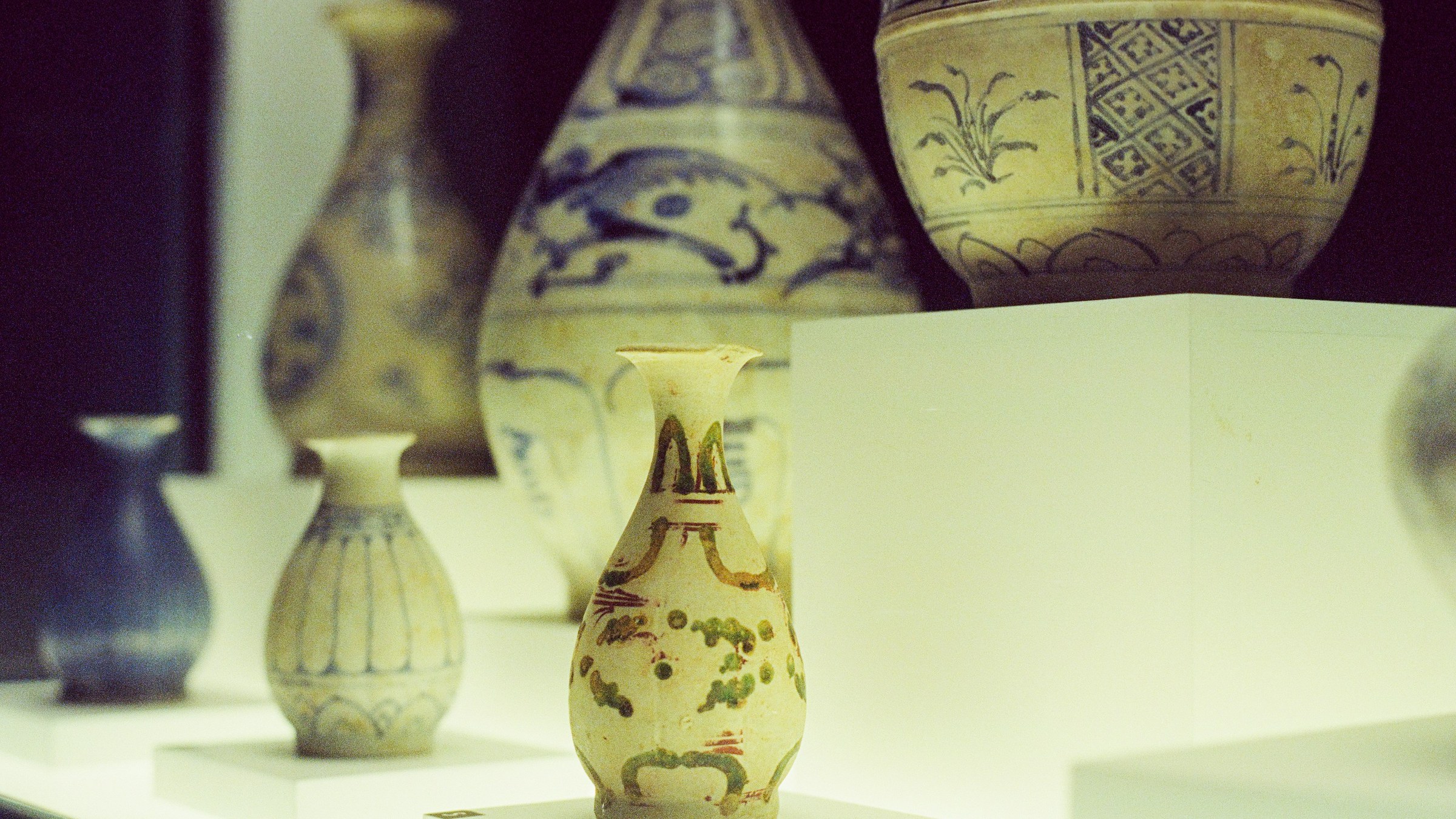 ガラスケース内に並ぶ古代アジアの青花磁器と多色絵磁器の展示。手前に絵付けの梨形小瓶、奥に複数の壺・瓶・碗。歴史博物館の典型的な収蔵展示の俯瞰寄りクローズアップ。