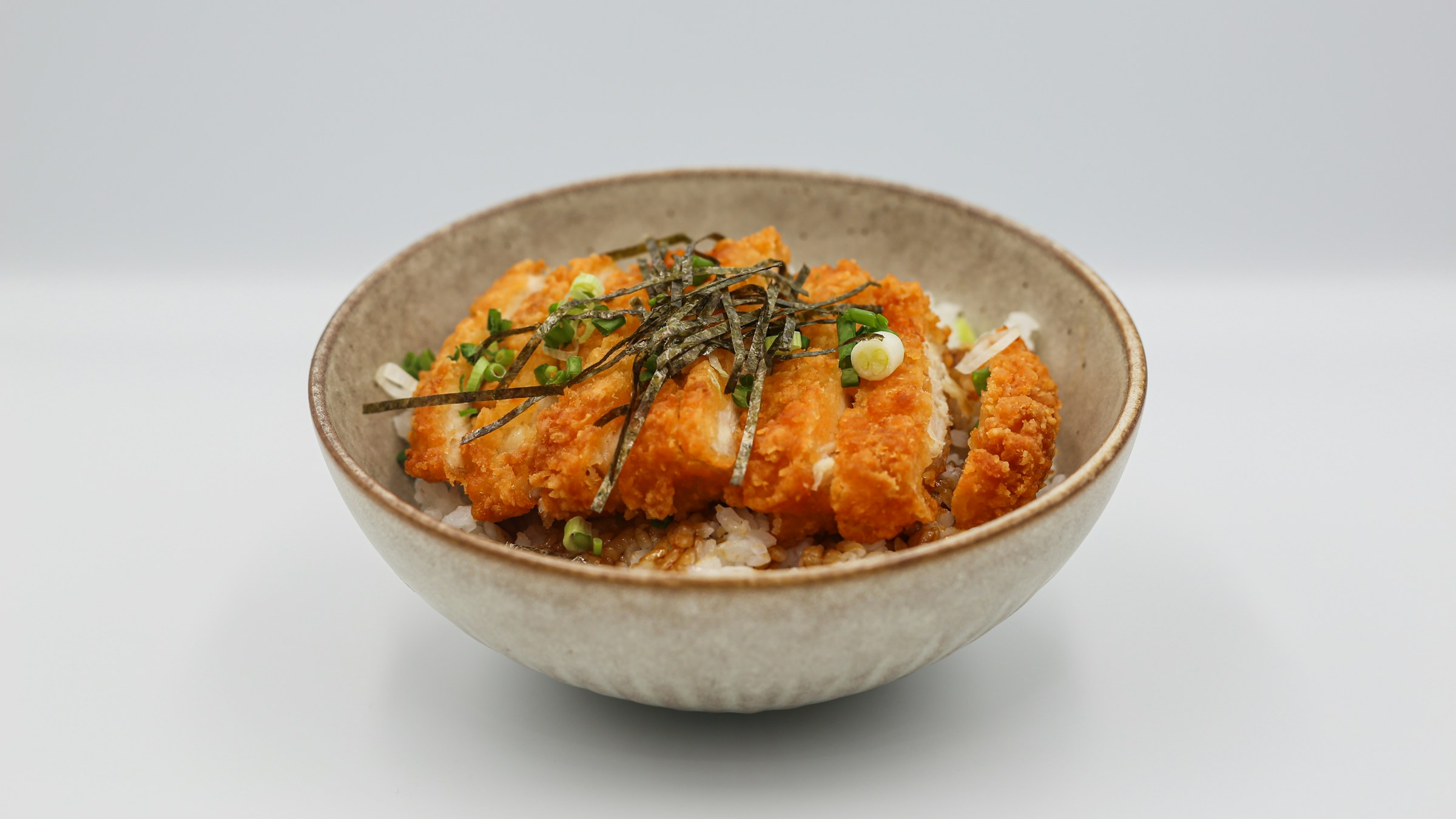 ベージュ色のストーンウェア丼に盛られたカツ丼/ソースカツ丼。とんかつの上に刻みノリ、刻みネギ、ごま、ソースのドリズル。とんかつの派生型(カツ丼/カツカレー等)を象徴する一枚。