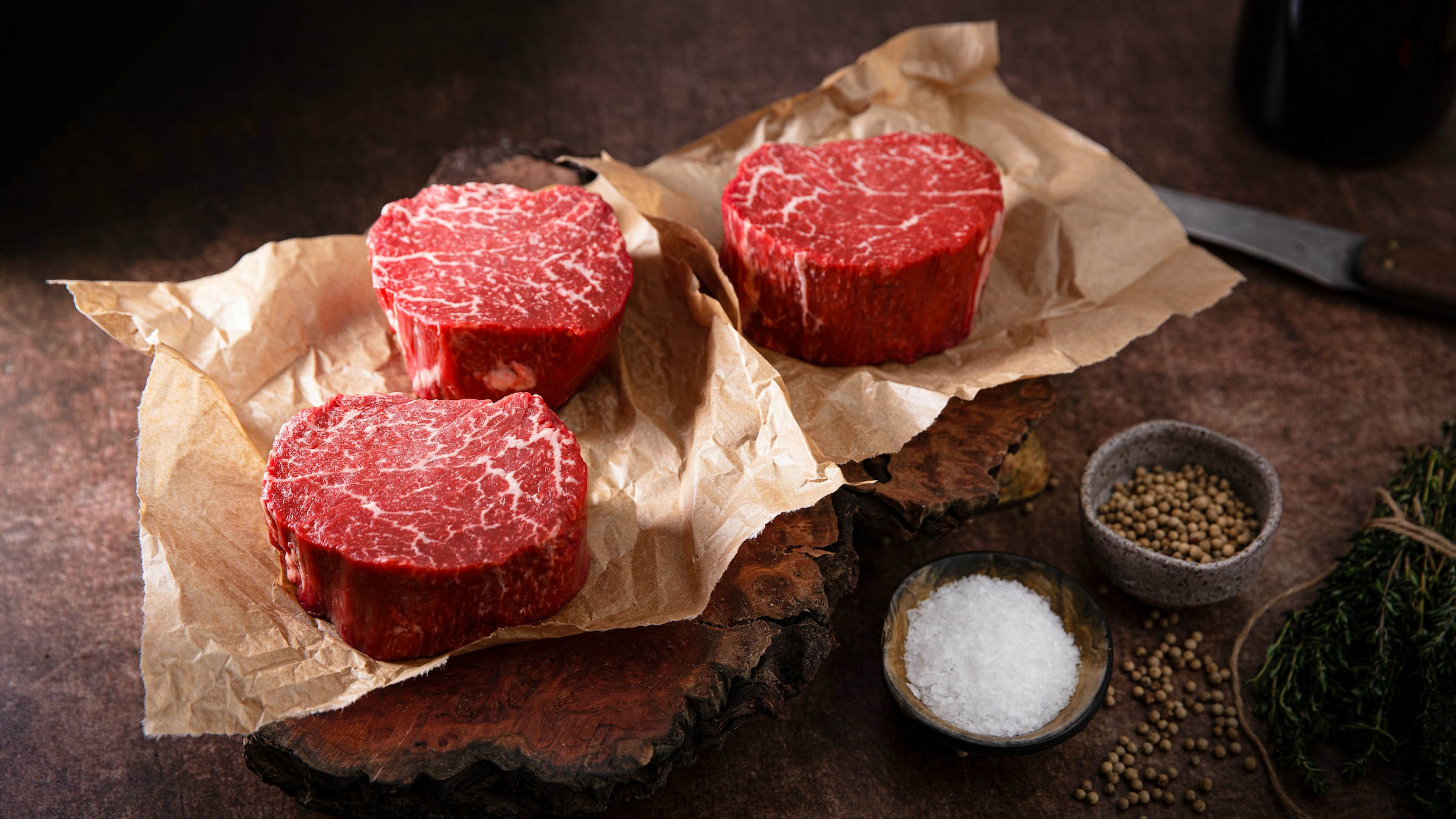 クラフト紙の上に並ぶ厚切りの霜降り牛肉と、岩塩や粒胡椒のスパイス類。銘柄牛・wagyu のクオリティを象徴する一枚。