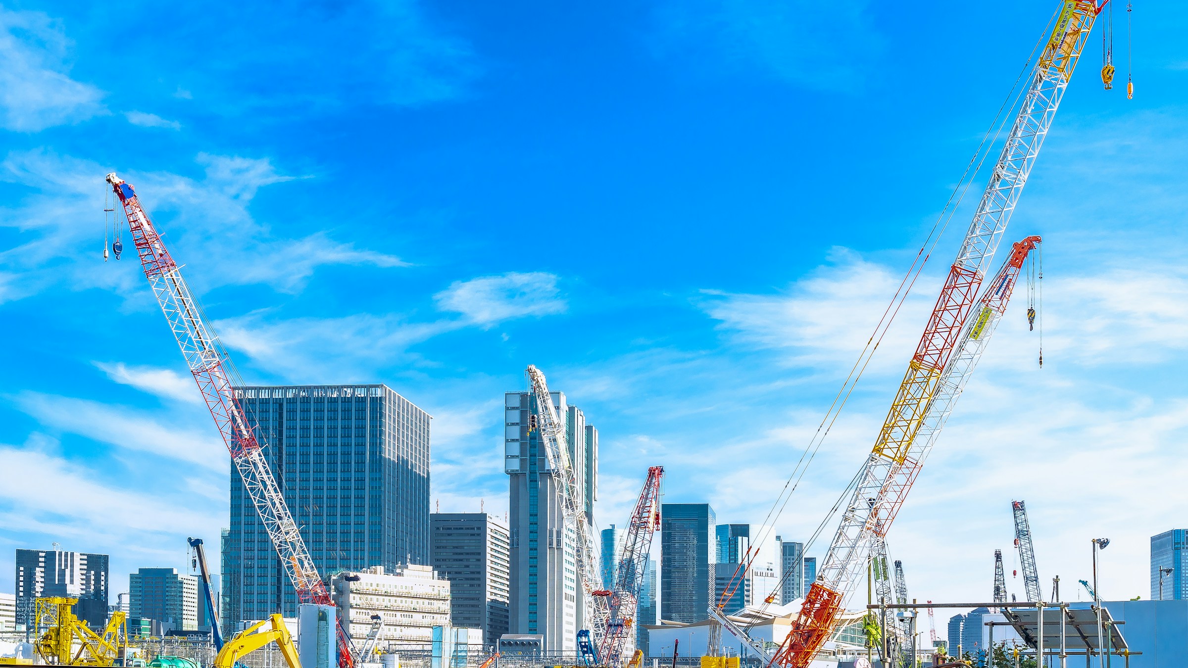 日本の都市部に立ち並ぶ建設現場のクレーン群と高層ビル。