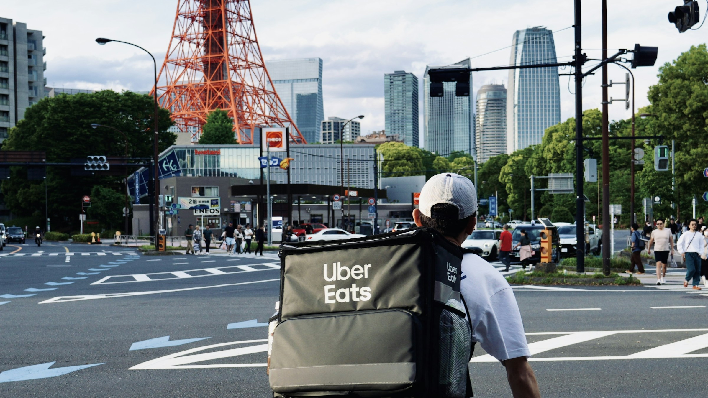 東京タワーを背景に、横断歩道で信号待ちをするUber Eatsの自転車配達員。