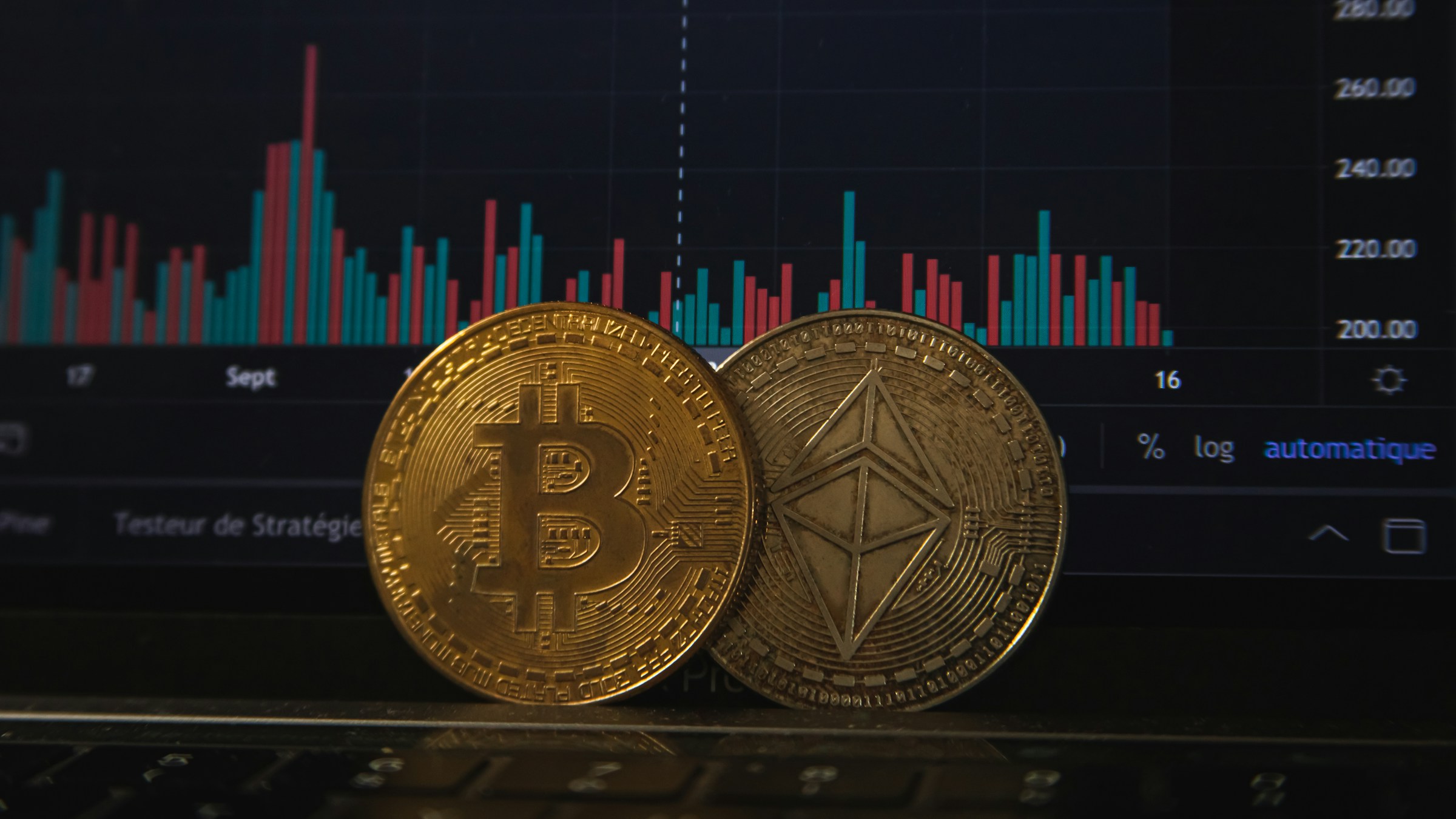 BitcoinとEthereumのコインを、トレーディングチャートを背景に並べた構図。