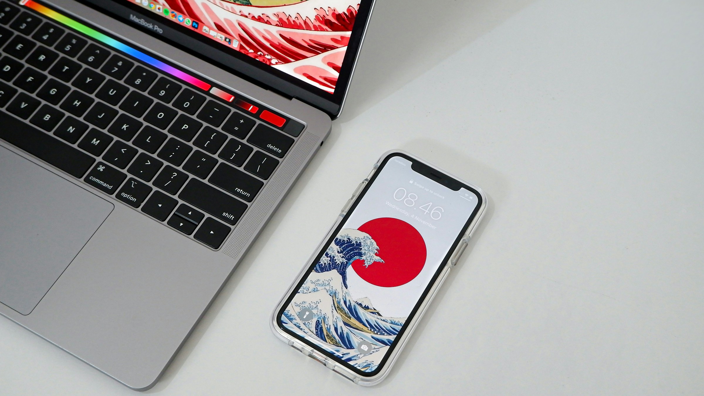 机に置かれたMacBook ProとiPhone。画面に日本の和柄壁紙が映る。